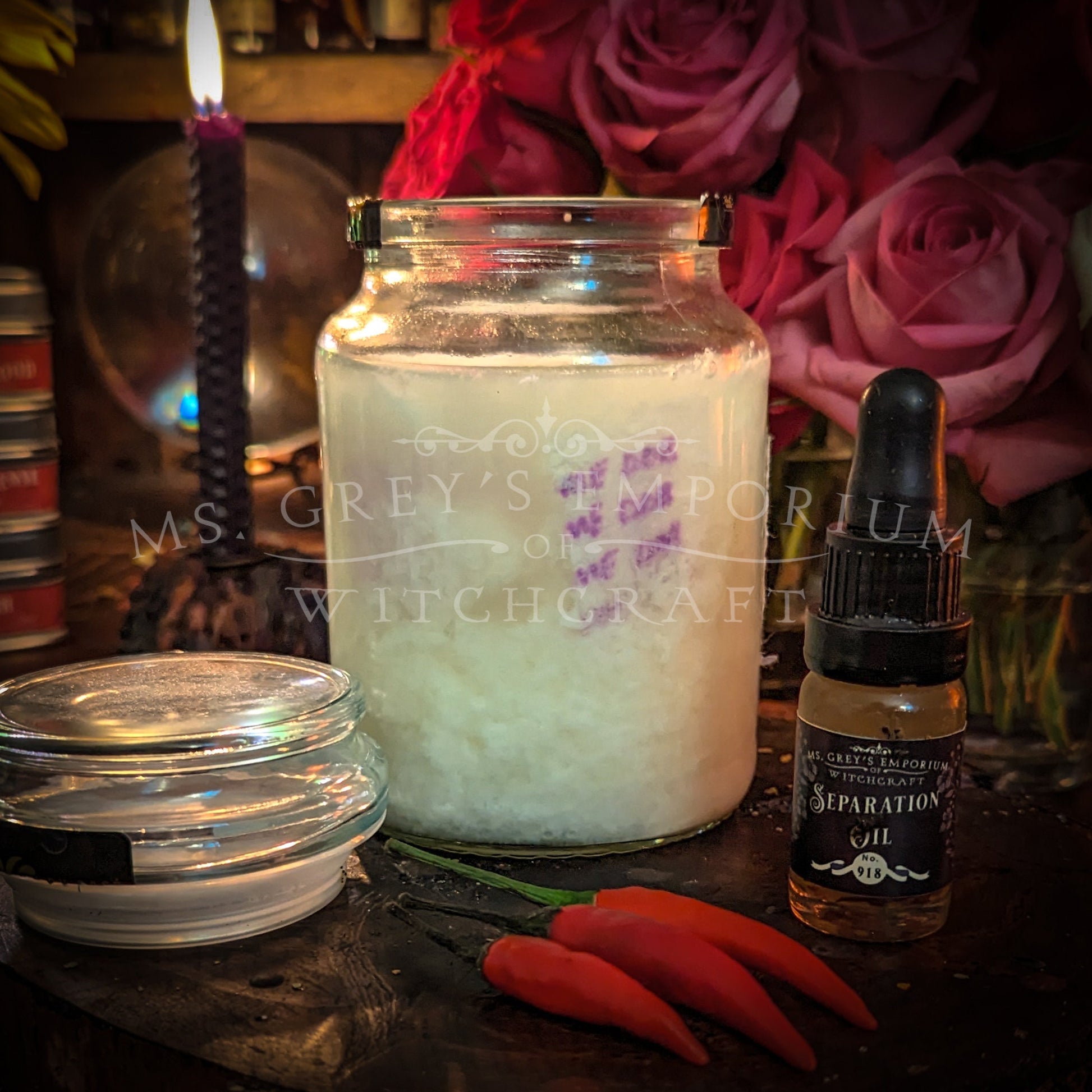 An old coffee jar filled with a curdled mixture and a torn in half name paper. The jar ispictured with three hot chillies and a little bottle of separation conjure oil. There is a lit purple candle in the background.